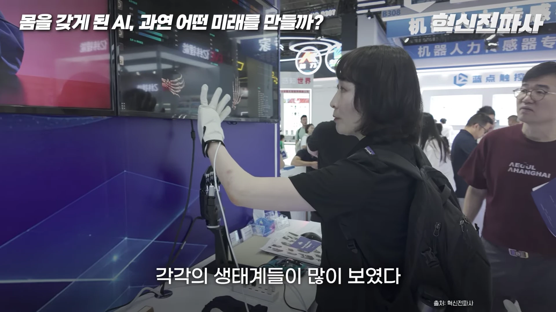 전시회 부스에서 한 사람이 모션 캡처 장갑을 끼고 화면에 비친 로봇 손 모델을 제어하고 있으며, 주변에는 관련 기술 장비들이 배치되어 있다.