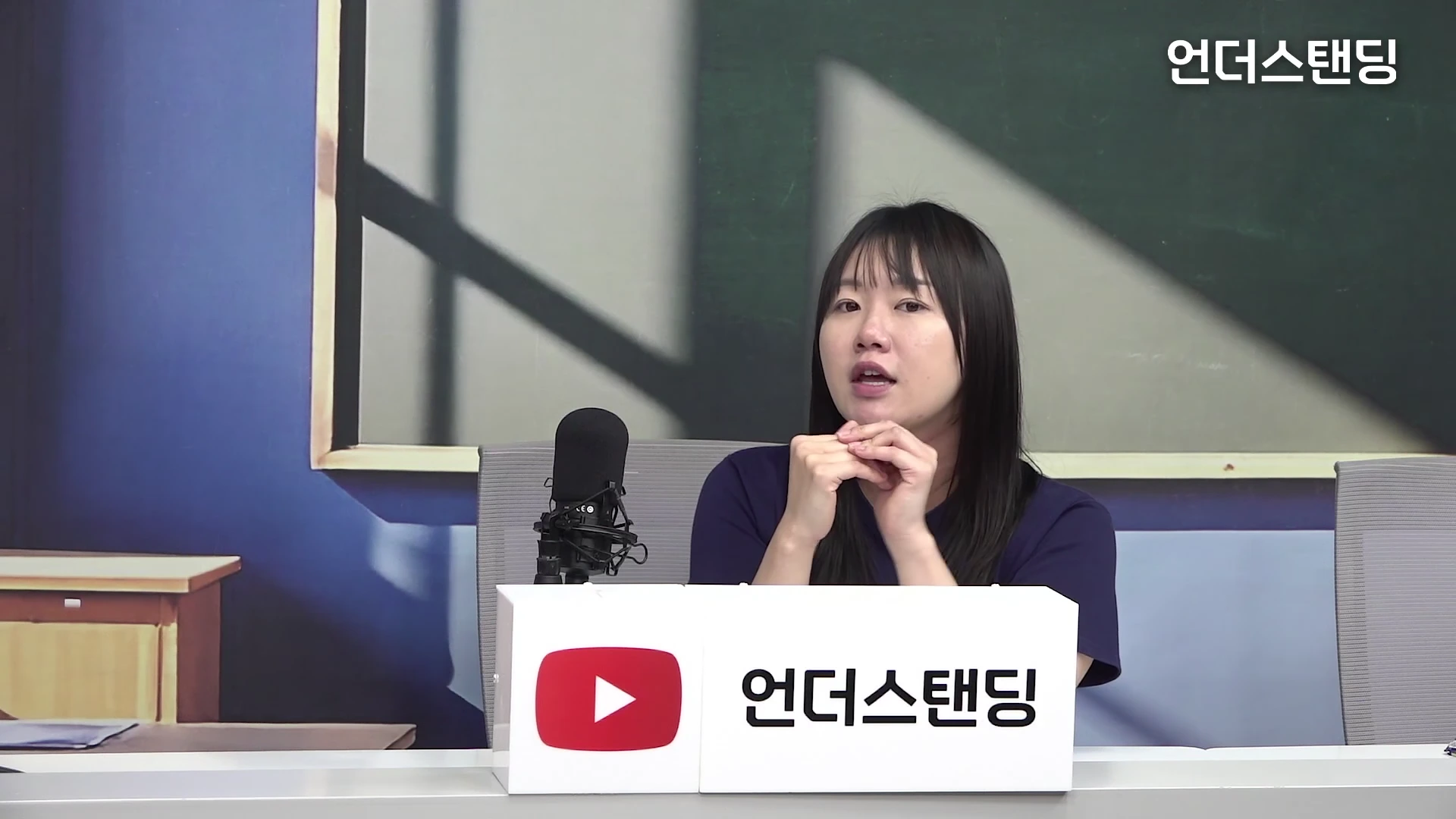 스튜디오에 앉아 마이크 앞에 대고 이야기하는 한 여성의 모습.
