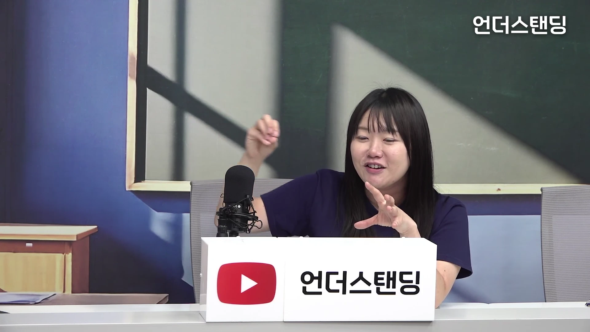 스튜디오에 앉아 있는 긴 생머리 여성이 마이크 앞에서 손짓하며 대화하는 모습