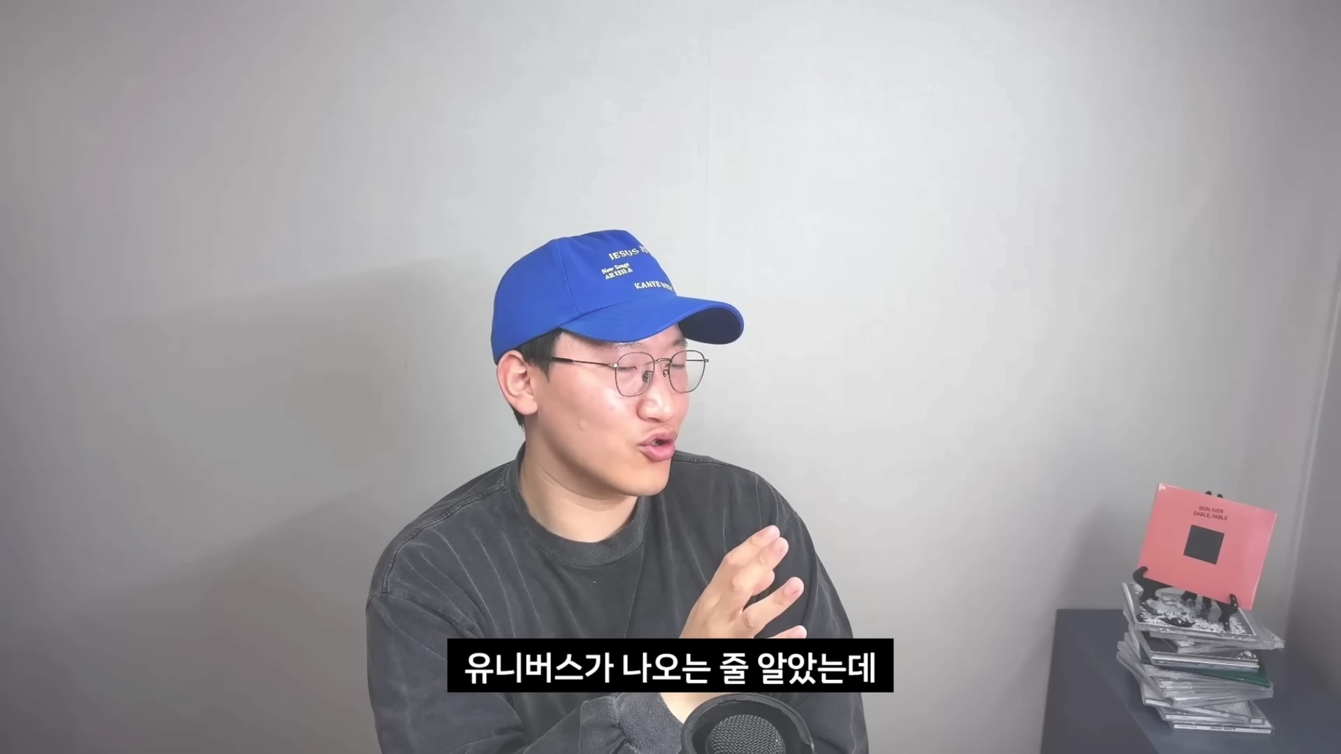 파란색 야구 모자와 안경을 쓴 남성이 마이크 앞에서 이야기하고 있으며 화면 하단에는 '유니버스가 나오는 줄 알았는데'라는 한글 자막이 있다.