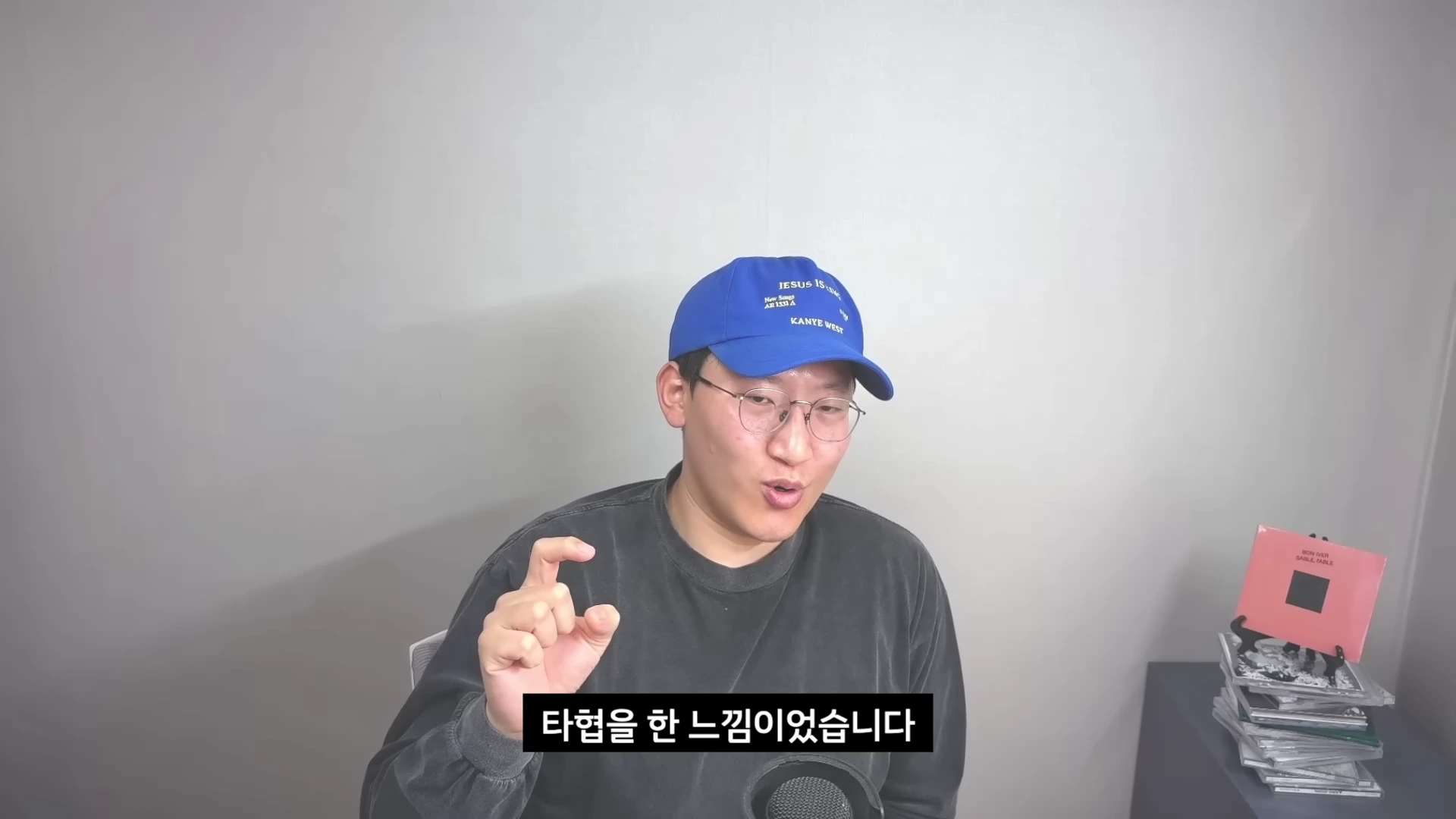 파란색 야구 모자와 안경을 쓴 남성이 밝은 배경 앞에서 손동작을 하며 이야기를 하고 있는 모습으로, 하단에는 한국어 자막이 삽입되어 있습니다.