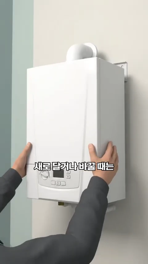 양손으로 벽에 설치된 흰색 가정용 보일러의 옆면을 잡고 있는 모습.