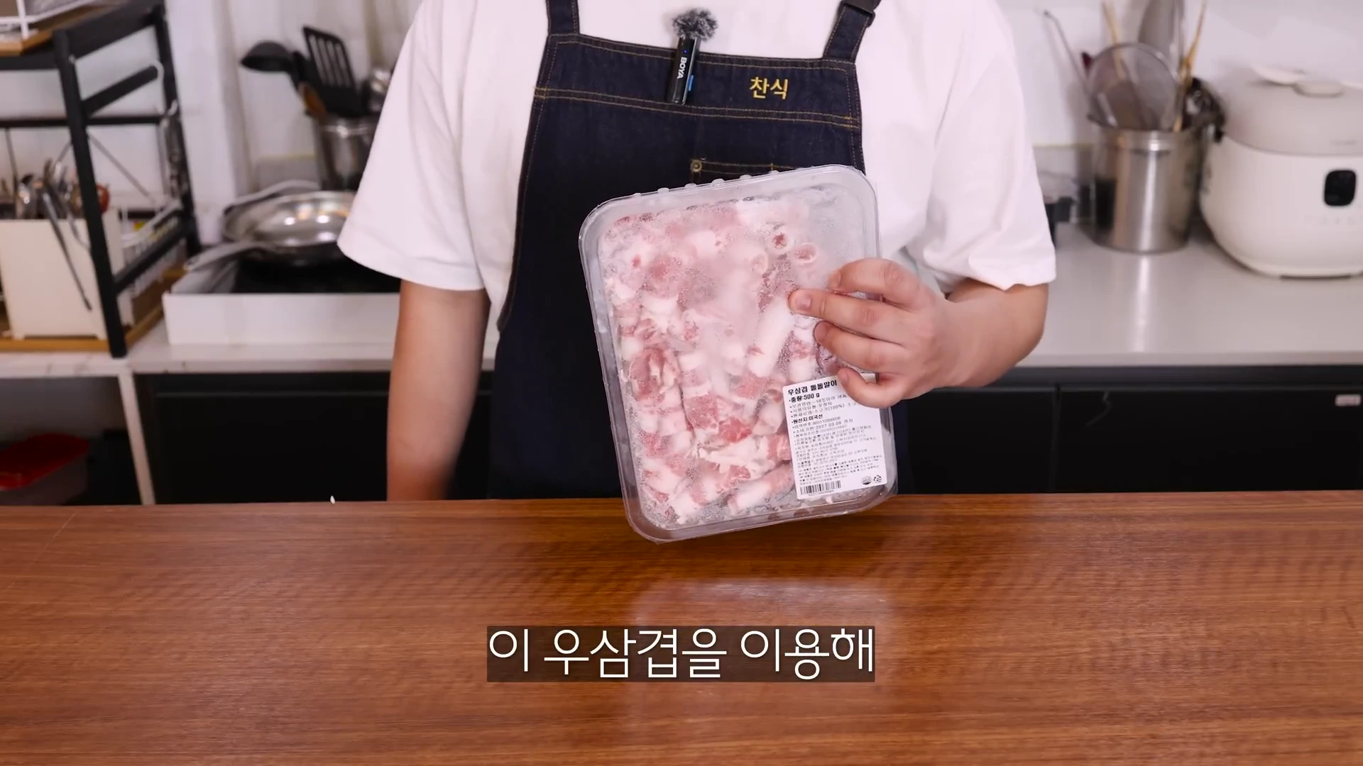 앞치마를 두른 요리사가 손에 냉동 우삼겹 팩을 들고 있는 모습.