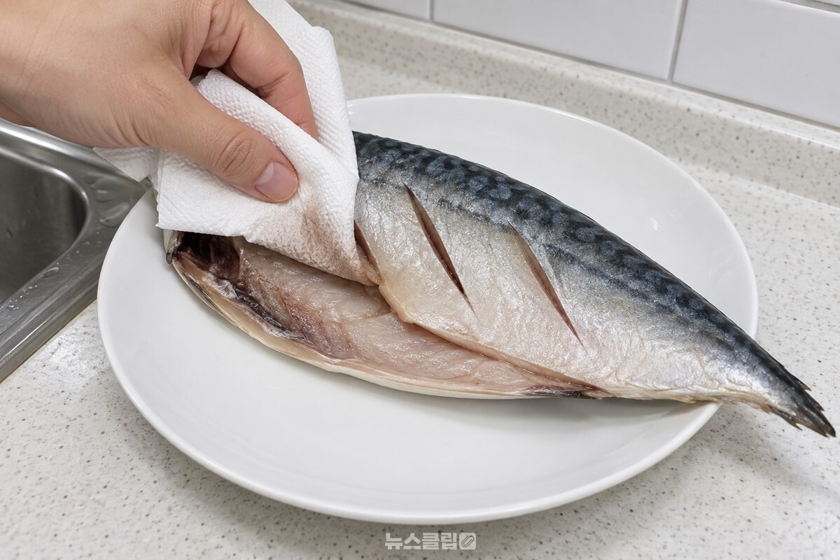 키친타월을 접어 고등어 배 속과 칼집 낸 자리를 눌러 가며 물기를 닦아 내는 손. / 기사 이해를 돕기 위한 생성형 이미지