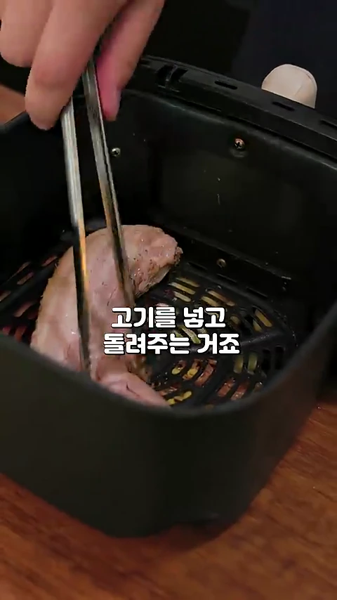 에어프라이어 바스켓 안에 집게를 사용하여 초벌 된 삼겹살을 담고 있는 모습이며 화면 중앙에는 고기를 넣고 돌려준다는 자막이 표시되어 있습니다.