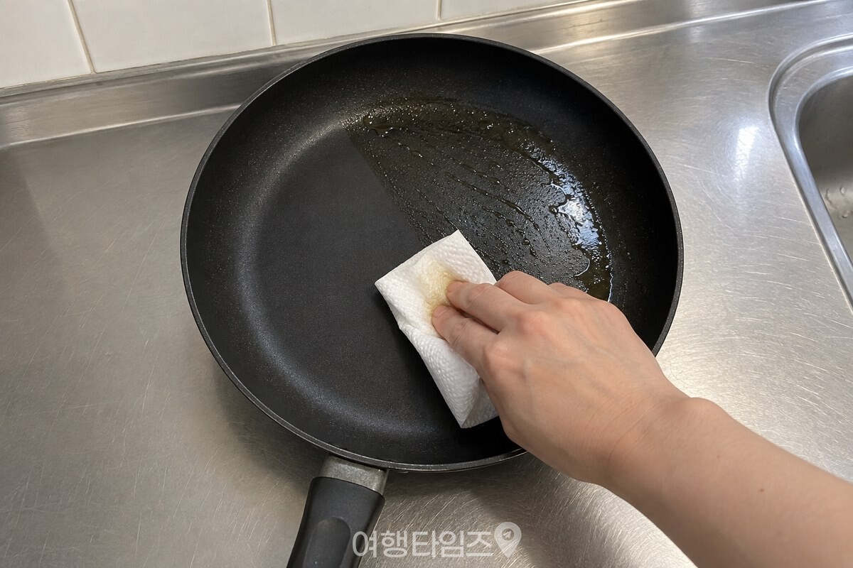 세제를 묻히기 전 검은 프라이팬 바닥을 접은 키친타월로 눌러 닦아 기름기를 걷어 내는 손. / 기사 이해를 돕기 위한 생성형 이미지