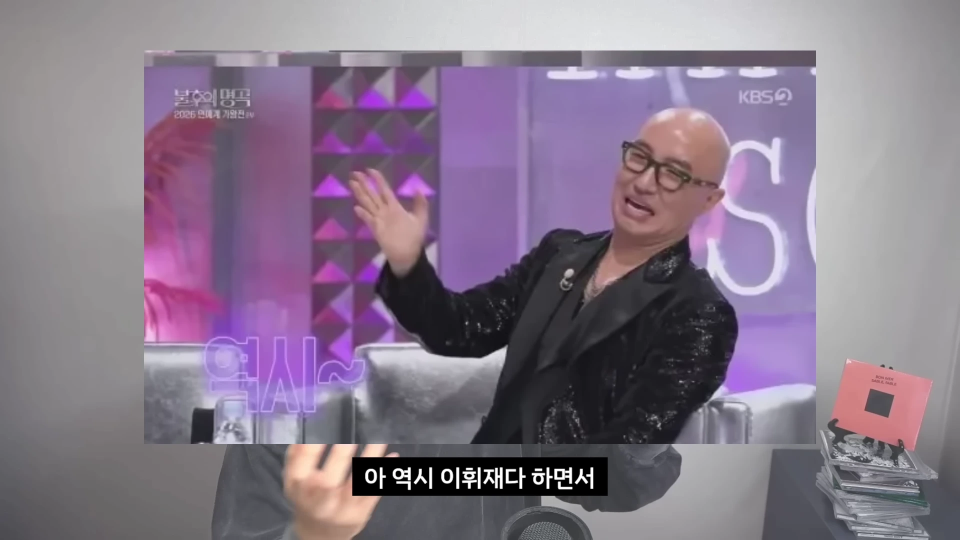 방송 화면 속에 안경을 쓴 민머리의 남성이 한쪽 손을 들고 웃고 있는 모습과 하단 자막에 '역시'라는 글자가 표기된 장면