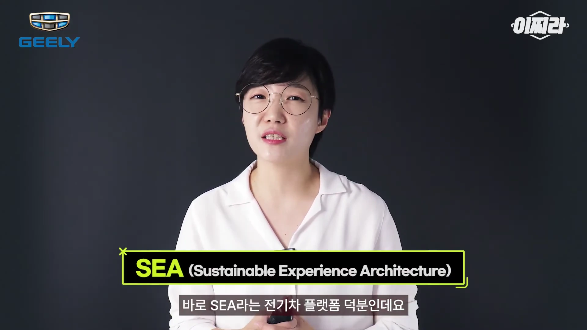검은색 배경 앞에서 흰색 셔츠를 입고 안경을 쓴 여성이 말하고 있으며, 화면 하단에는 'SEA (Sustainable Experience Architecture)'라는 문구와 함께 자막이 표시된 영상 화면.