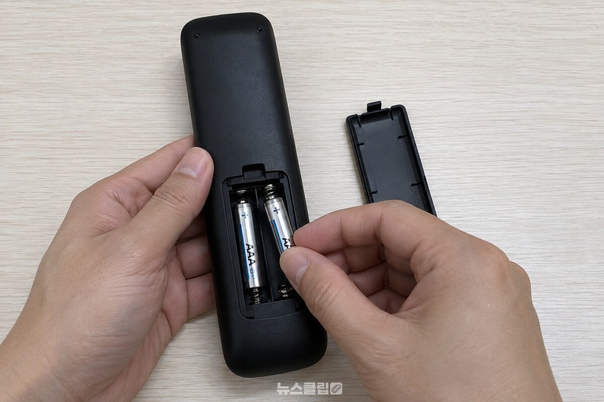 리모컨을 뒤집어 뒷면 건전지 뚜껑을 밀어 열고 AAA 건전지 두 개를 빼내는 모습. / 기사 이해를 돕기 위한 생성형 이미지