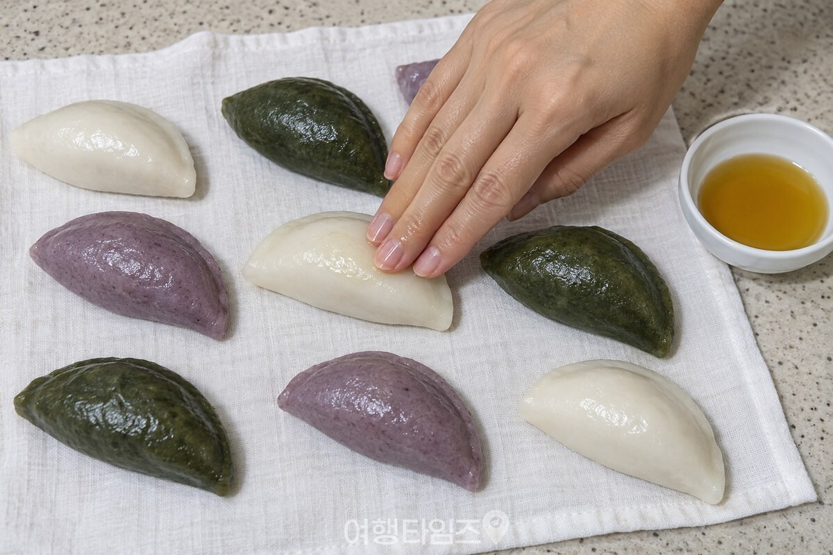 마른 흰 면포 위에 한 겹으로 펼친 송편에 참기름을 얇게 바르는 손 / 기사 이해를 돕기 위한 생성형 이미지