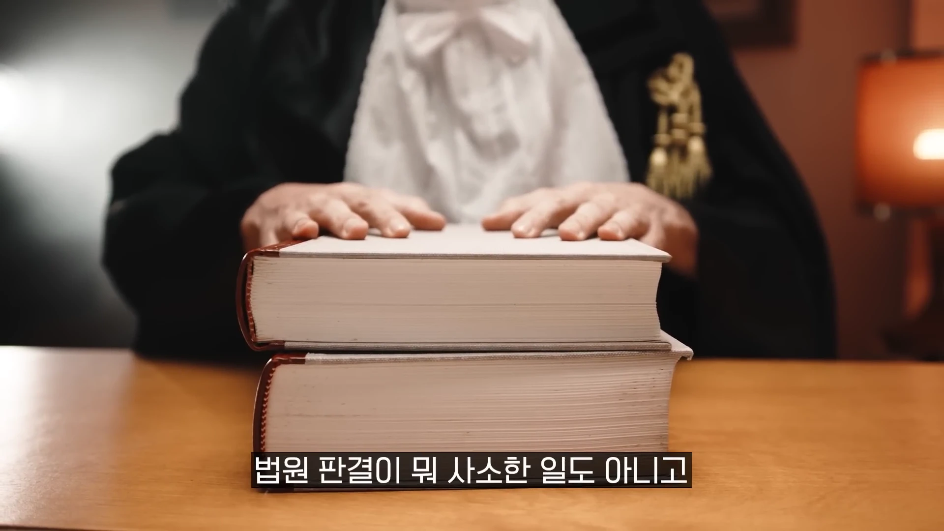 판사 복장을 한 사람이 두꺼운 법전 두 권 위에 손을 올리고 있는 모습이다.