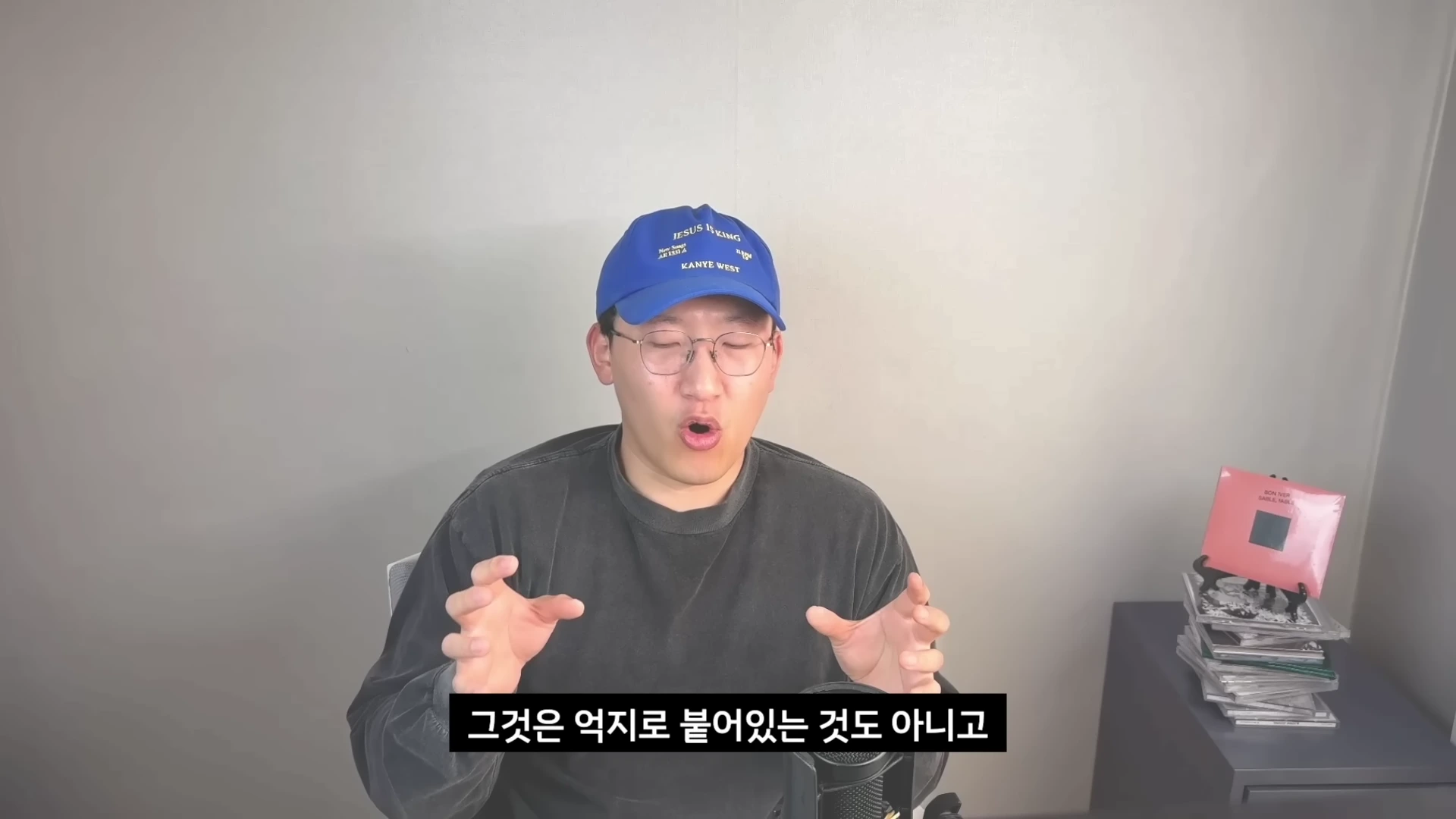 파란색 야구 모자와 안경을 착용한 남성이 마이크 앞에서 손동작을 하며 이야기하고 있으며 화면 하단에는 한국어 자막이 표시되어 있습니다.