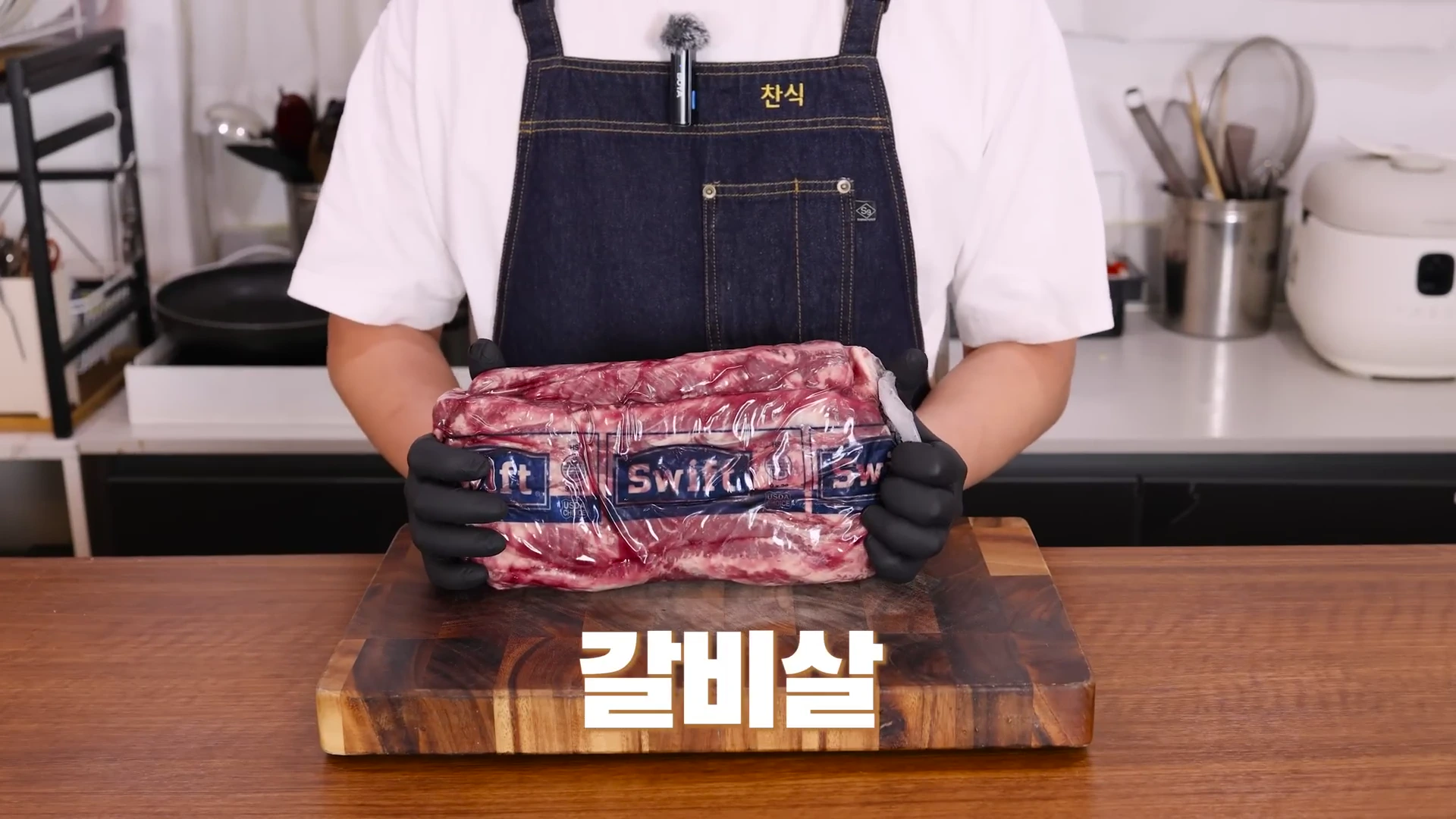 앞치마를 입고 검은색 위생 장갑을 낀 요리사가 진공 포장된 대용량 소고기 원육을 두 손으로 들어 보이고 있으며, 화면 하단에는 '갈비살'이라는 흰색 자막이 표시되어 있습니다.