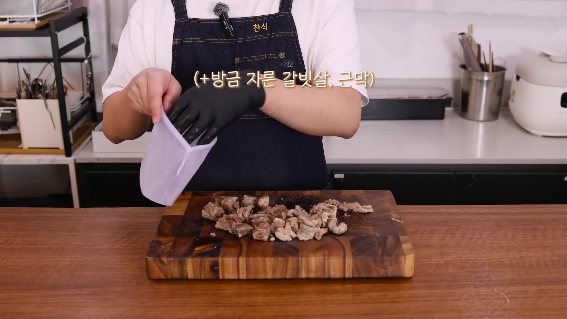 앞치마를 입고 검은색 위생 장갑을 낀 요리사가 나무 도마 위에 놓인 자른 갈빗살과 근막을 실리콘 지퍼백에 담고 있다.