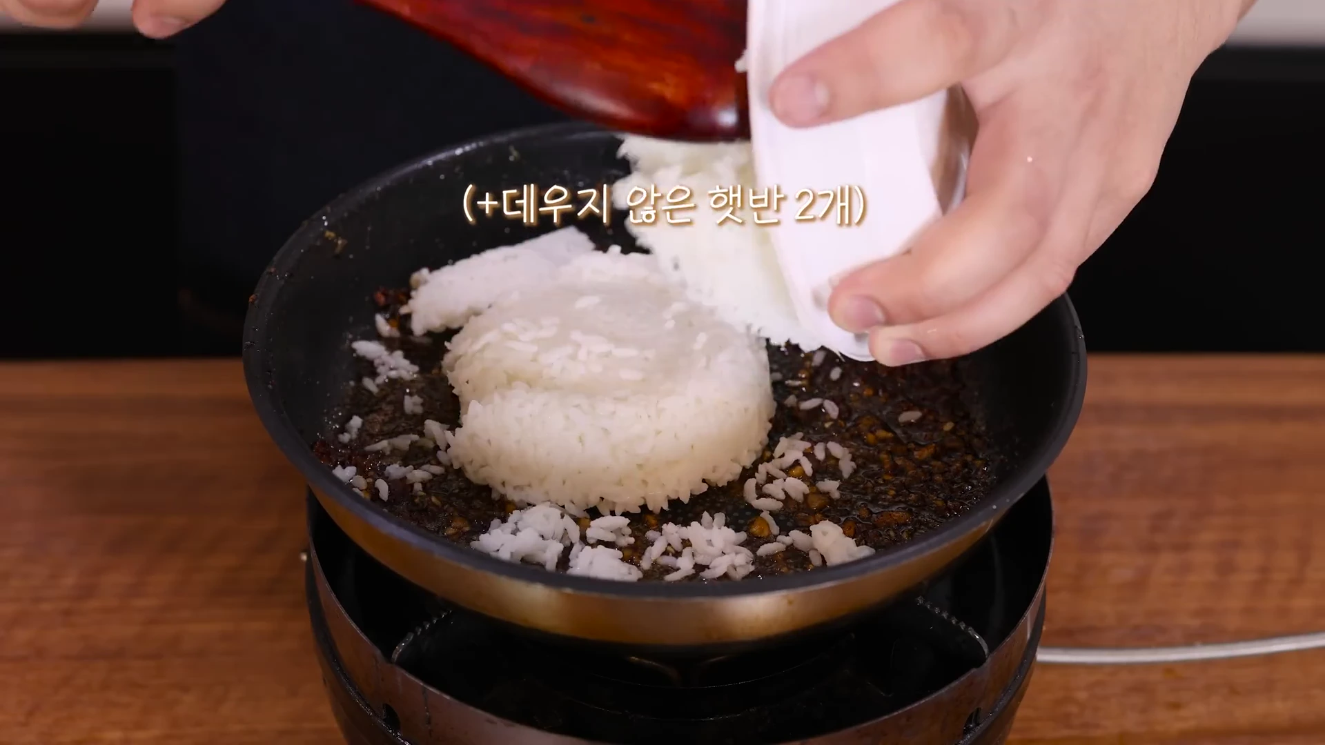 프라이팬에 고기를 구워 먹고 남은 양념 위에 데우지 않은 즉석밥 두 개를 넣는 모습