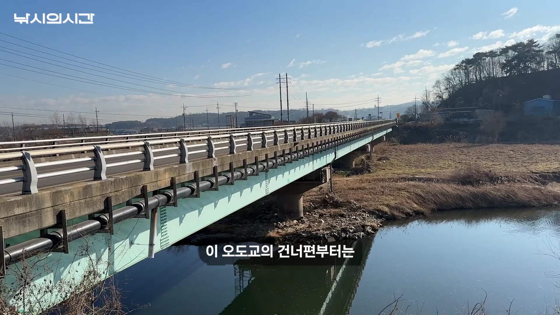 하천을 가로지르는 긴 교량과 그 아래 잔잔하게 흐르는 물가 풍경이 담긴 영상 속 장면으로 화면 중앙에는 '이 오도교의 건너편부터는'이라는 자막이 떠 있습니다.