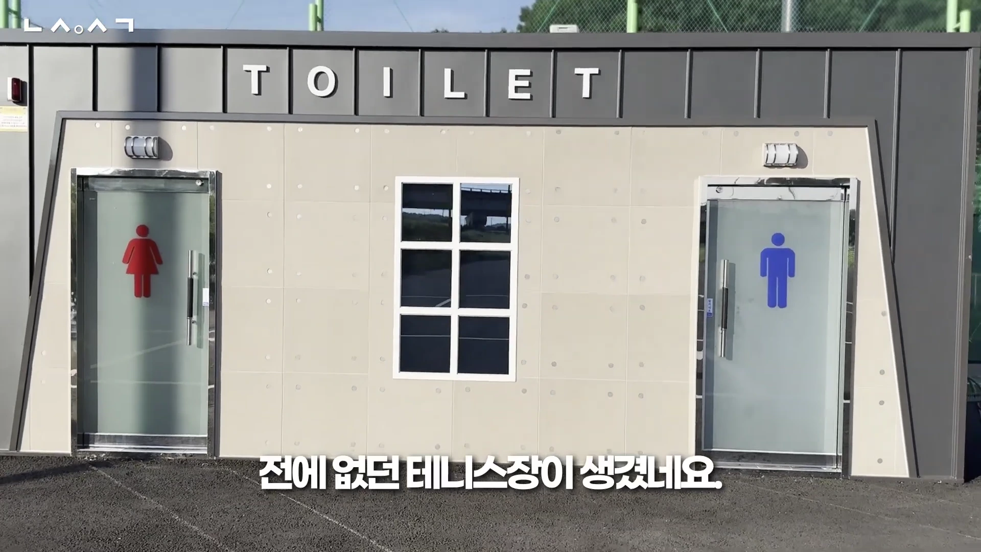 공중화장실 건물 외관 정면 모습. 남녀 화장실 출입구와 중앙의 격자창이 보이며 상단에 TOILET 글자가 적혀 있습니다.