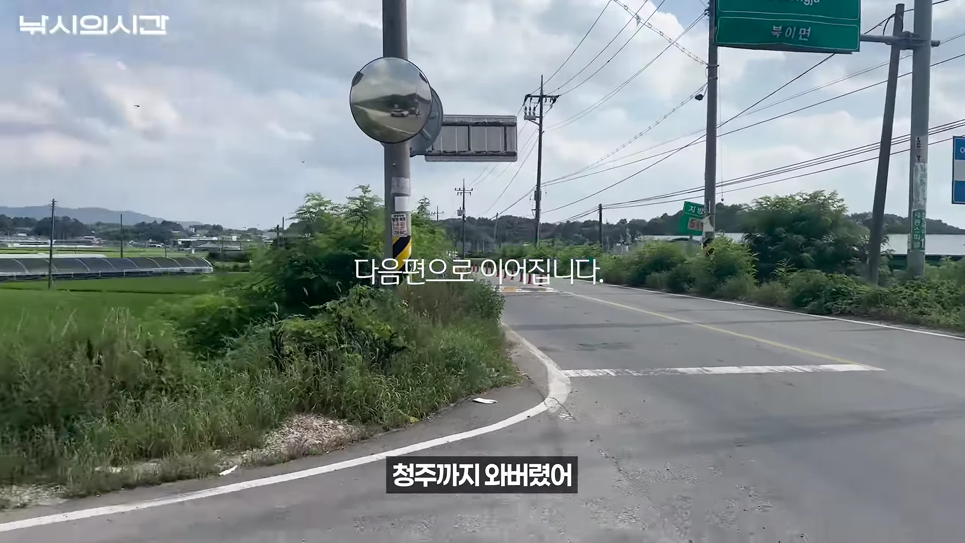 도로변에 설치된 볼록 거울과 이정표, 전신주가 보이는 시골길의 풍경입니다.