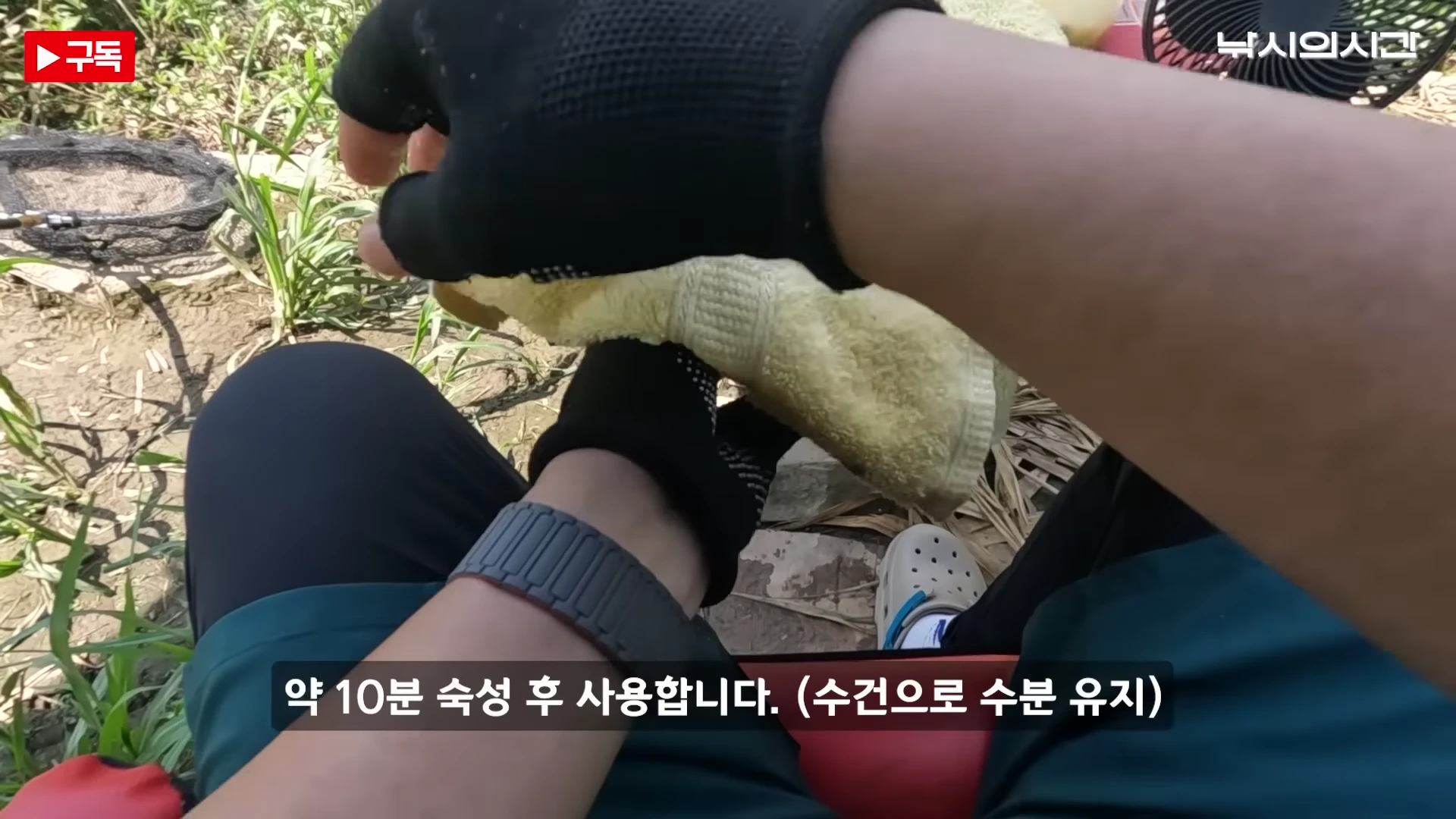 낚시꾼이 낚시터 바닥에 앉아 수건으로 떡밥 그릇을 덮어 숙성시키는 1인칭 시점의 영상 캡처 화면