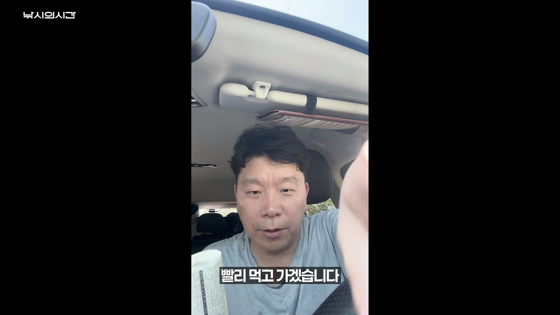 차량 운전석에 앉아 카메라를 응시하는 한 남성이 김밥을 들고 식사를 준비하는 모습