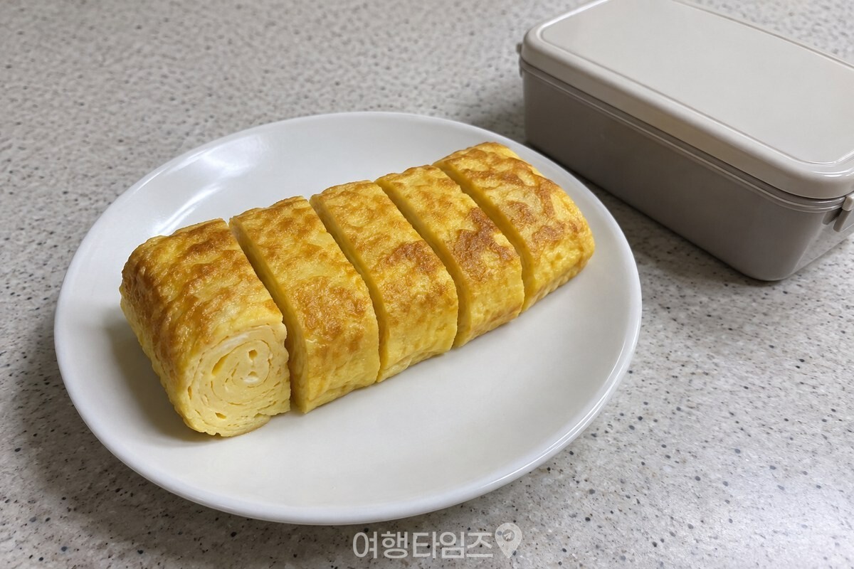 도시락 통 옆 접시에 두툼하게 썬 노란 계란말이가 놓여 있다. / 기사 이해를 돕기 위한 생성형 이미지