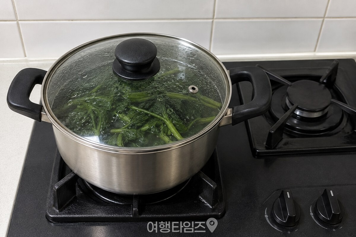 불을 끈 스테인리스 냄비에 유리 뚜껑을 덮어 삶은 취나물을 그대로 두고 뜸을 들이는 모습. / 기사 이해를 돕기 위한 생성형 이미지