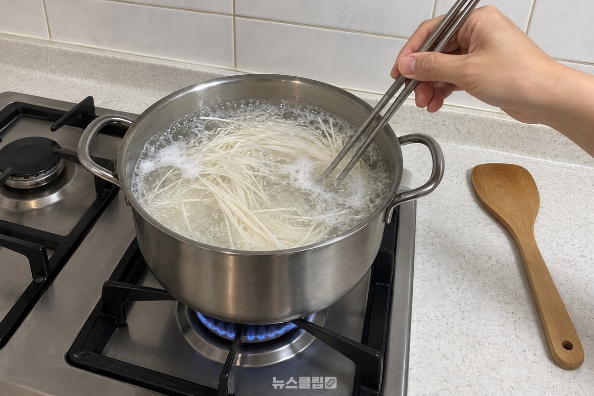끓는 물에 넣은 소면을 젓가락으로 한 번 저어 면을 풀어 주고 있고, 주걱은 냄비 옆 조리대에 놓여 있다. / 기사 이해를 돕기 위한 생성형 이미지