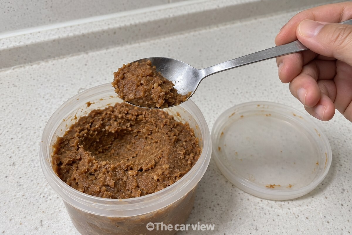 밥숟가락에 된장이 절반 정도 담겨 있고, 아래에는 뚜껑을 연 된장통이 놓여 있다. / 기사 이해를 돕기 위한 생성형 이미지