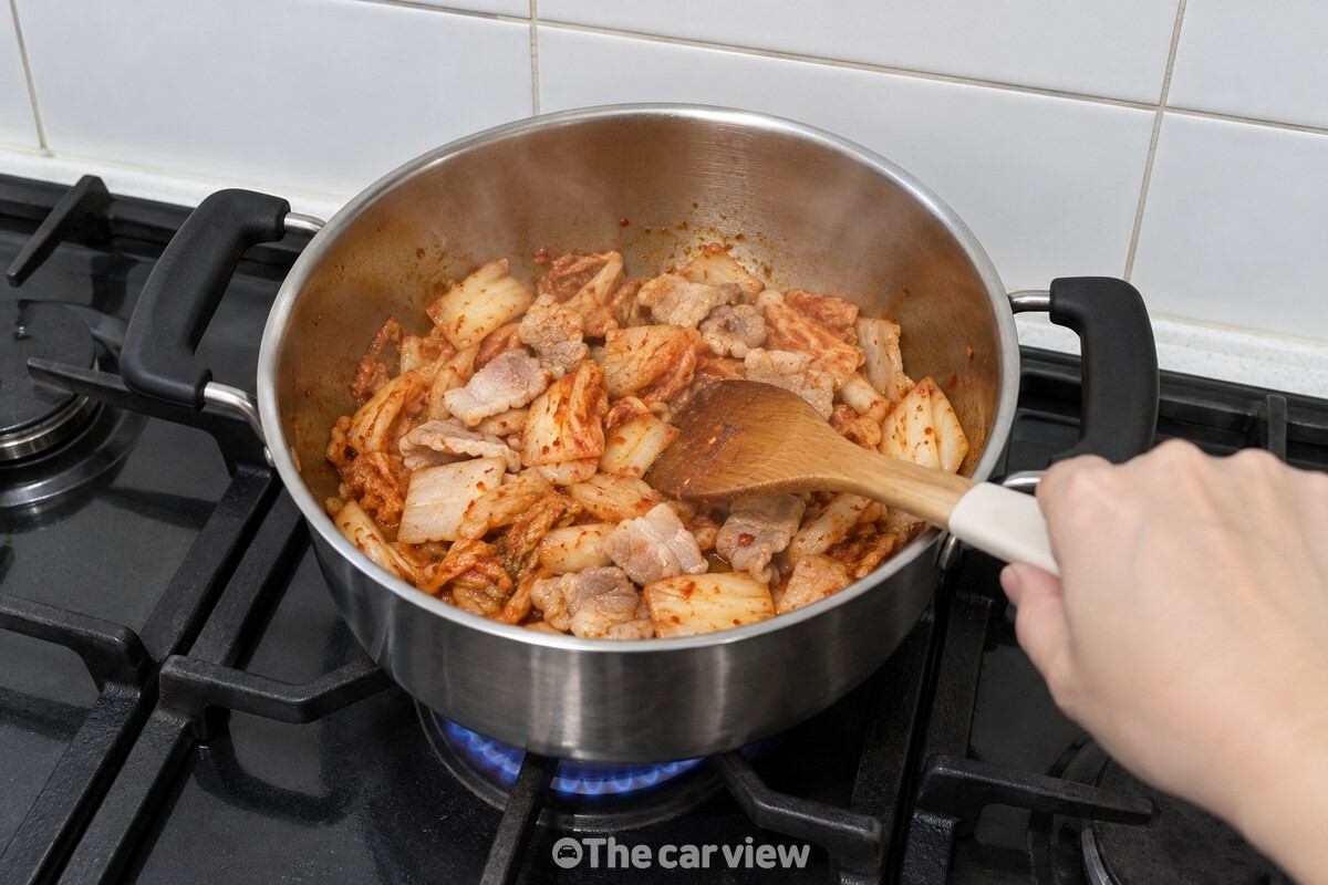 냄비 안에서 썰어 넣은 김치와 돼지고기가 기름에 볶이며 고기 겉면이 하얗게 변하고 있다. / 기사 이해를 돕기 위한 생성형 이미지