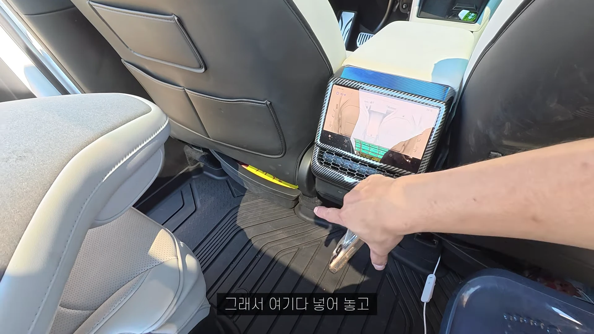 테슬라 차량의 2열 센터 콘솔 하단에 설치된 작은 수납함에 손을 넣어 물건을 정리하고 있는 모습
