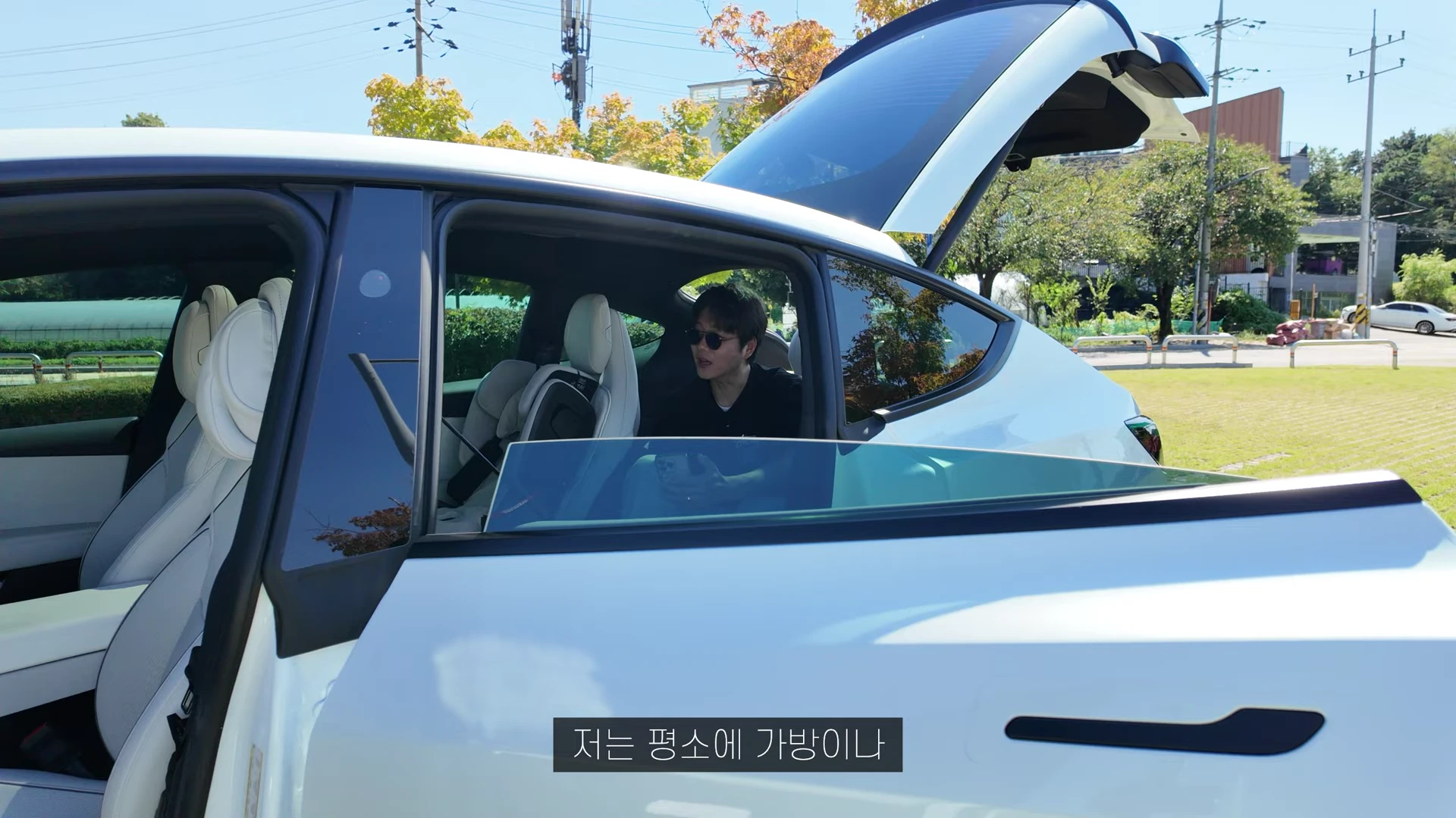 흰색 전기 SUV의 열린 뒷좌석 문을 통해 안쪽 좌석과 카시트가 보이고, 운전석에 앉은 남성이 뒤를 돌아보며 이야기하는 모습