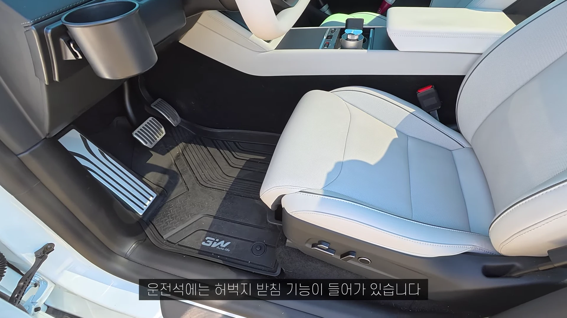 테슬라 차량의 내부 운전석 시트와 바닥 매트가 보이는 모습으로, 허벅지 받침 기능이 강조된 시트의 하단 조절 버튼과 바닥에 설치된 전용 매트가 보입니다.