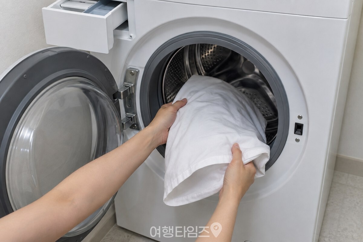 벗긴 베개 커버를 드럼세탁기 문 안으로 넣는 손. / 기사 이해를 돕기 위한 생성형 이미지