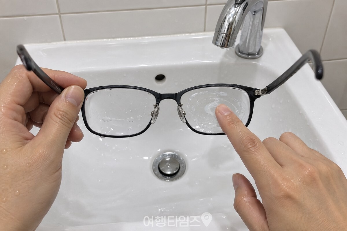 세면대 앞에서 한 손에 든 검은 뿔테 안경의 렌즈 양면에 다른 손 손가락으로 주방세제를 펴 바르는 모습. / 기사 이해를 돕기 위한 생성형 이미지