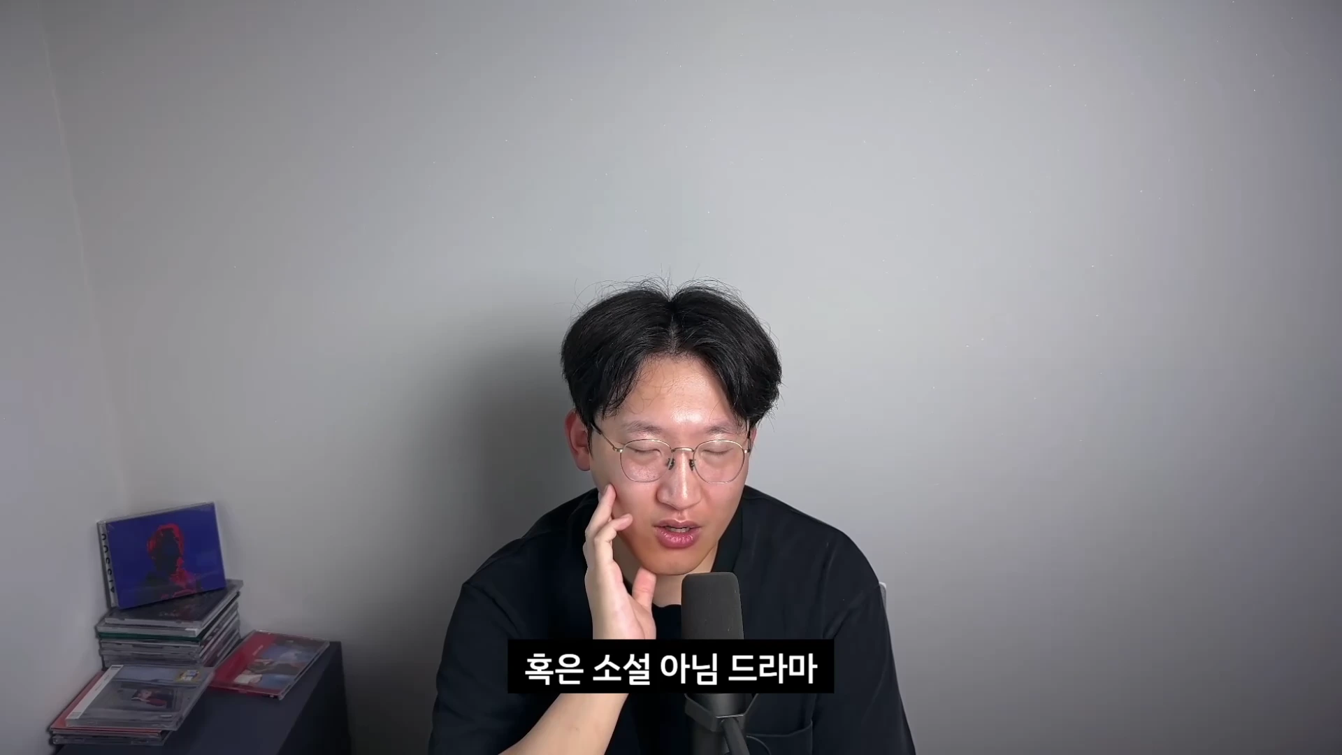 안경을 쓴 남성이 마이크 앞에 앉아 생각에 잠긴 표정으로 턱을 괴고 있으며 화면 하단에는 한국어 자막이 표시되어 있습니다.