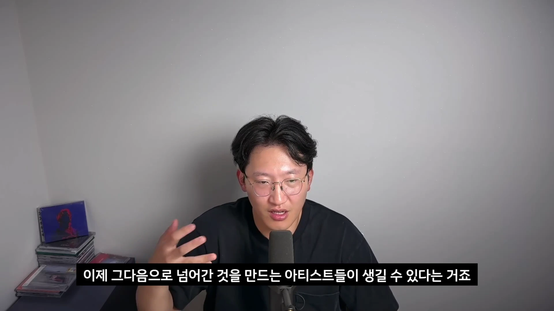 검은색 티셔츠를 입고 안경을 쓴 남성이 마이크 앞에서 대화하는 모습과 영상 하단에 한국어 자막이 표시된 화면입니다.