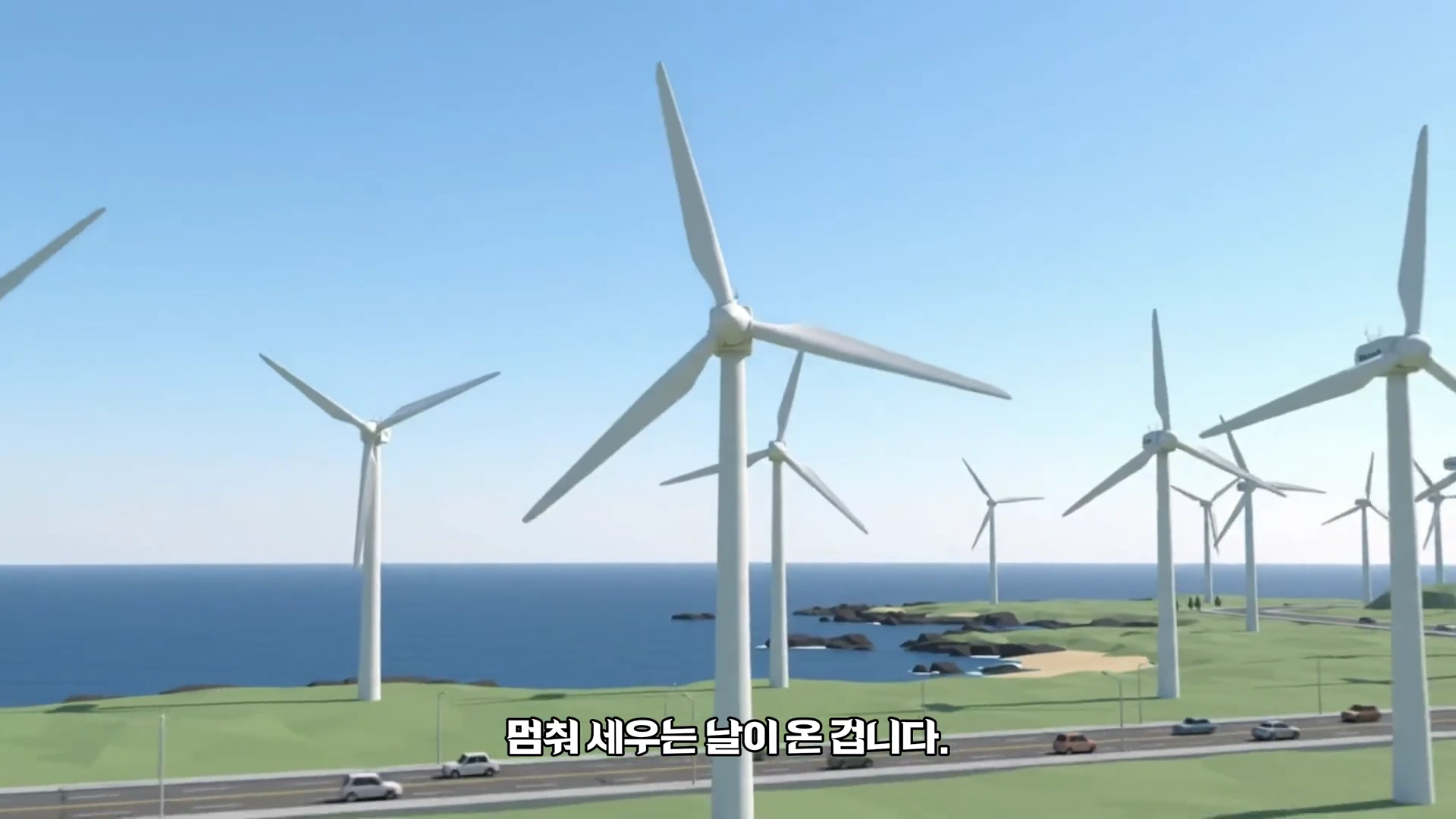 푸른 바다를 배경으로 해안 도로 옆 초지에 설치된 여러 개의 거대한 풍력 발전기 모습.