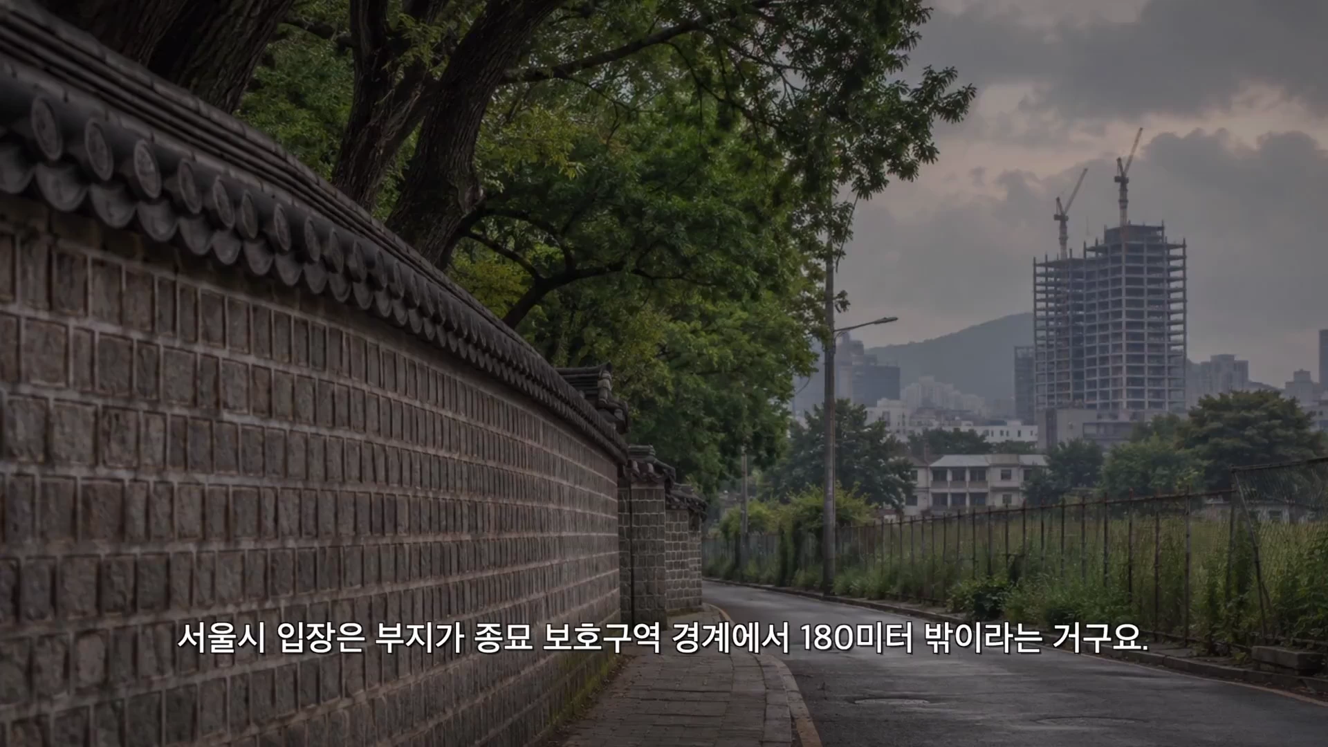 서울의 고즈넉한 돌담길 옆으로 낡은 울타리와 나무가 보이고, 멀리 고층 건물이 건설 중인 풍경이 담겨 있다.