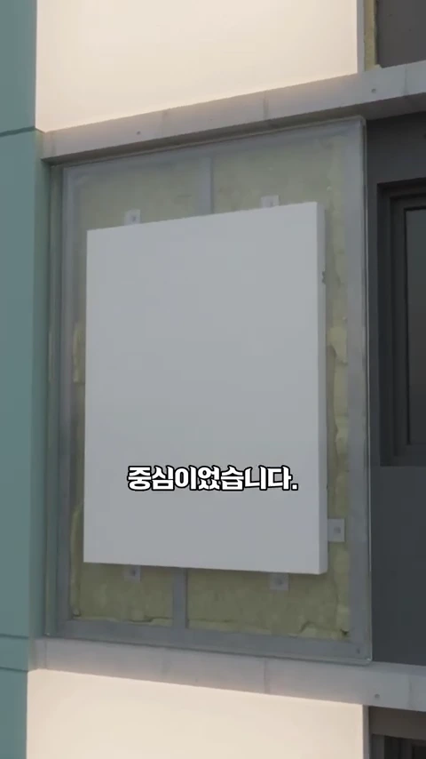 공사 중인 건물의 외벽에 사각형 단열재가 부착되어 있는 모습이며, 화면 중앙에는 '중심이었습니다.'라는 자막이 표시되어 있습니다.