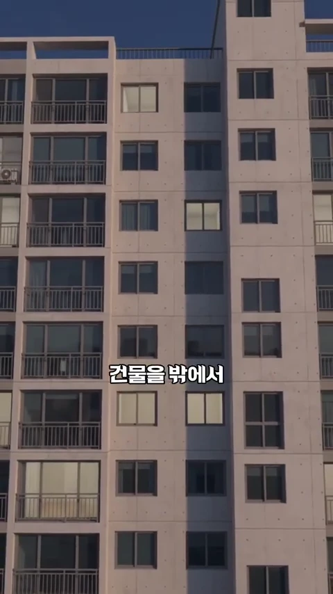 정면에서 바라본 아파트 외벽의 모습으로 규칙적으로 배치된 창문들과 콘크리트 구조가 보이며 '건물을 밖에서'라는 한글 자막이 화면 중앙에 나타나 있다.