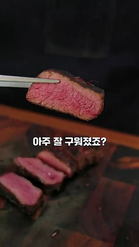 금속 집게로 잘 익은 미디엄 템포의 스테이크 단면을 들어 올리고 있는 모습이며 하단에는 먹기 좋게 썰린 고기들이 놓여 있습니다.