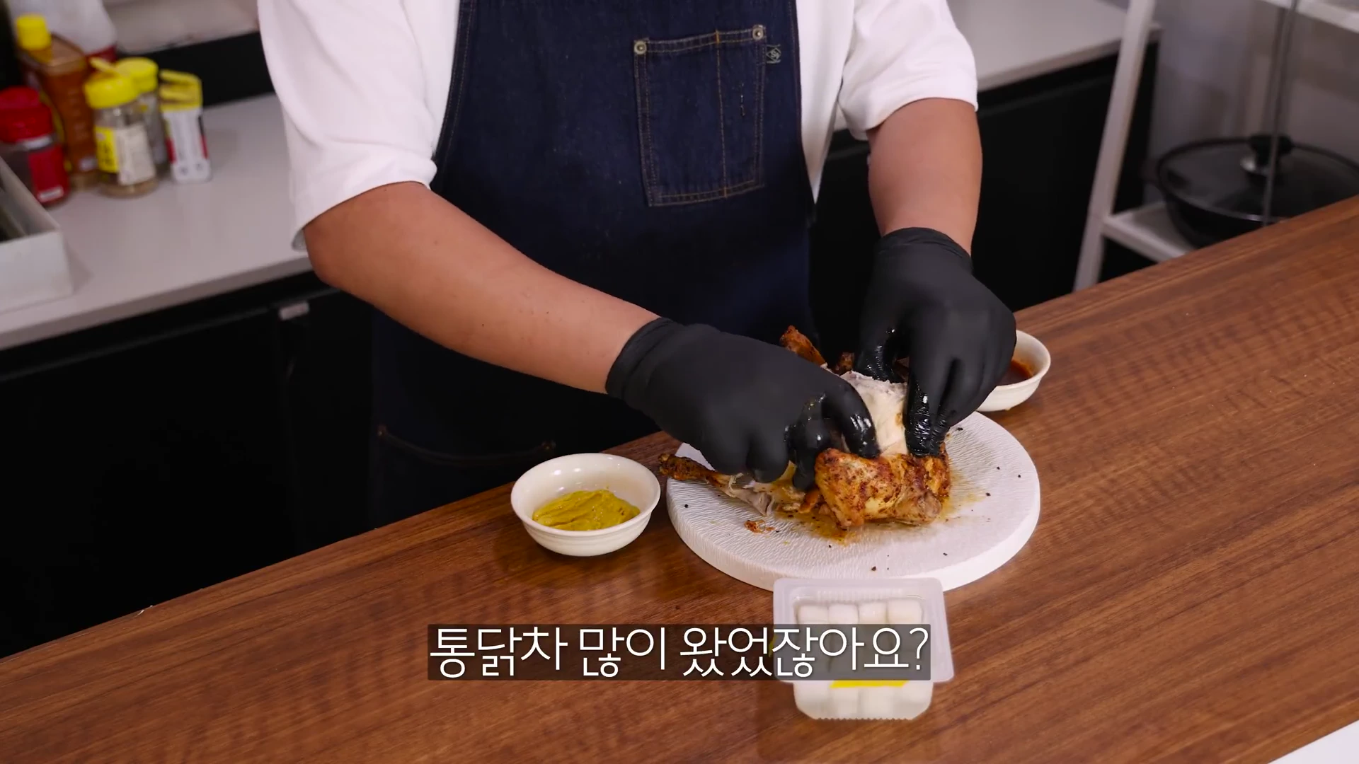 앞치마를 두르고 검은색 위생 장갑을 낀 요리사가 나무 식탁 위에서 완성된 구운 통닭을 손으로 해체하고 있다.