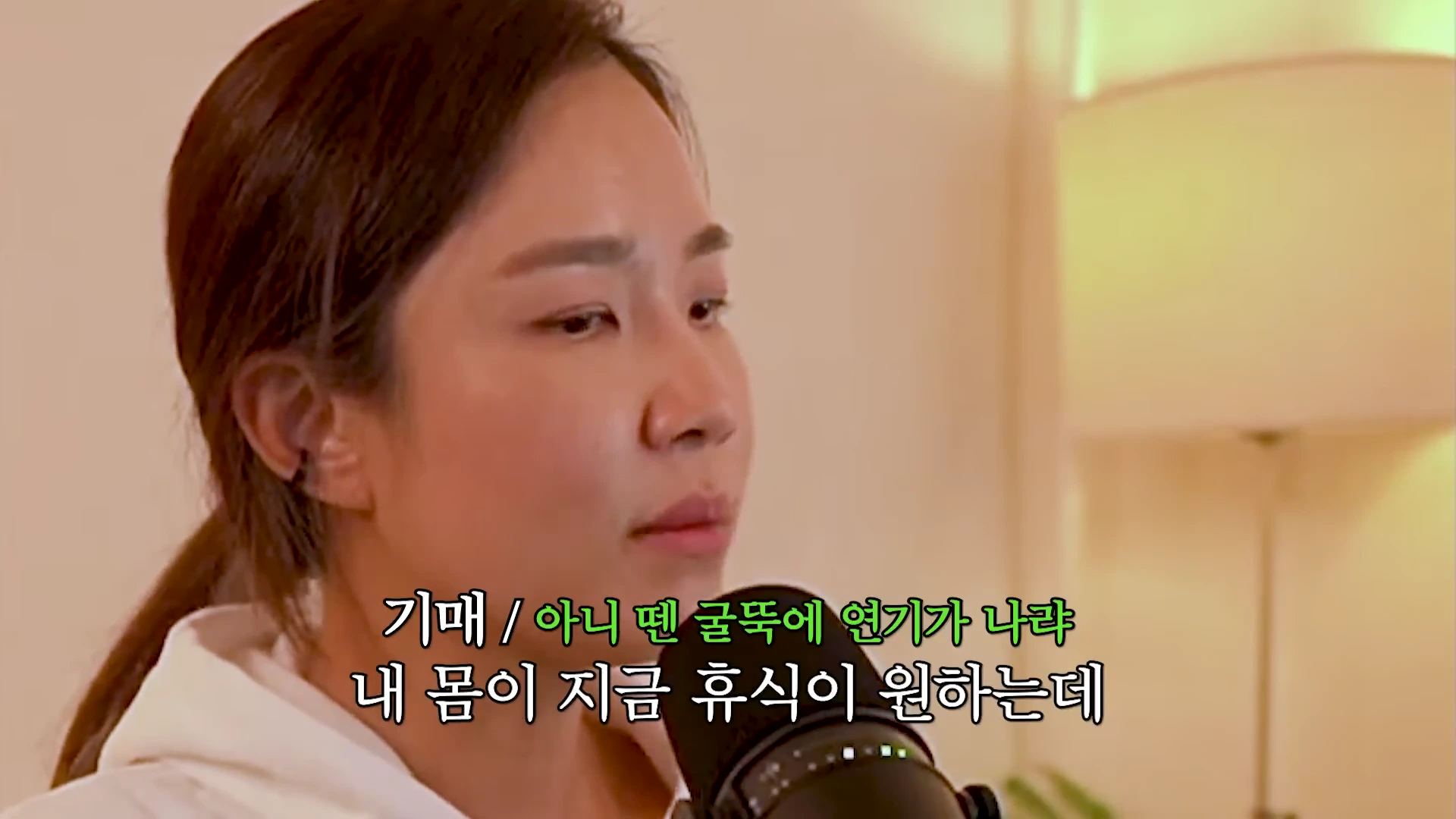 실내에서 검은색 마이크를 잡고 이야기를 나누고 있는 한 여성의 클로즈업 영상 화면.