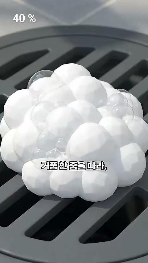 베란다 바닥 배수구 덮개 위로 하얀 세탁 거품이 뭉쳐 올라와 있는 모습이 담긴 근접 촬영 영상 프레임입니다.