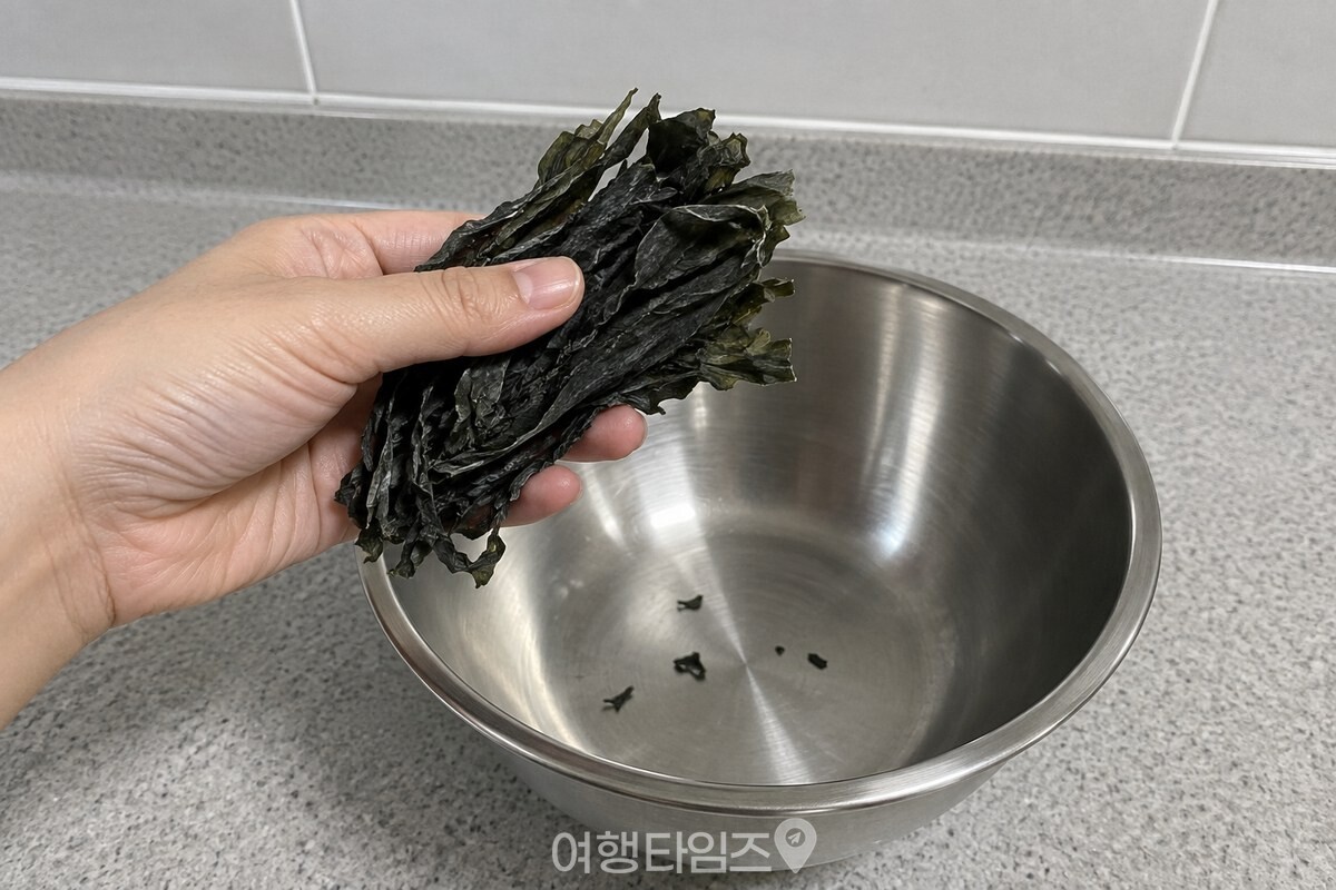 손으로 한 줌 집은 마른미역을 스테인리스 볼 위에서 들어 보이는 모습. / 기사 이해를 돕기 위한 생성형 이미지