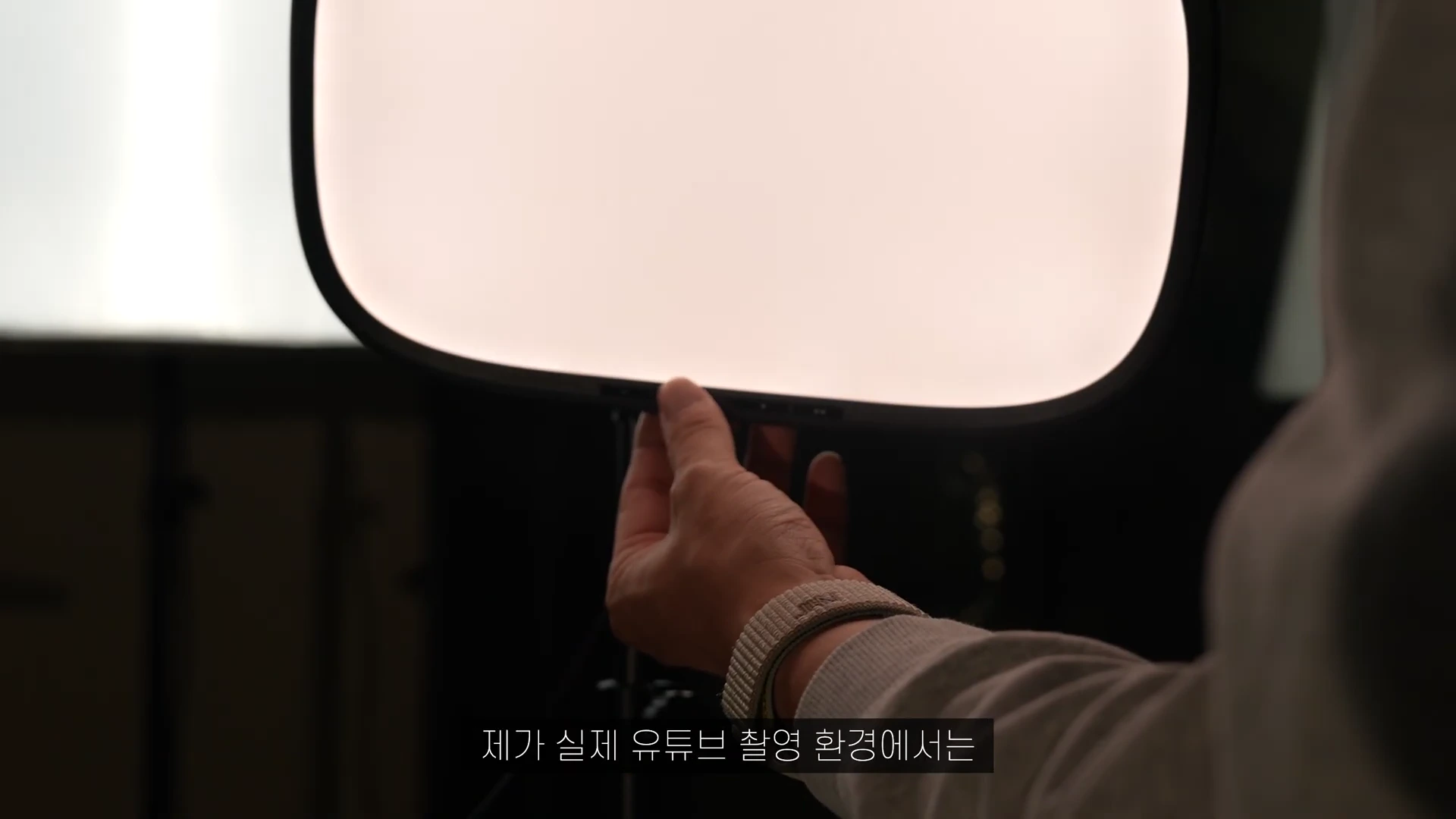 한 손이 켜져 있는 사각형의 LED 패널 조명 하단부를 조절하고 있는 모습