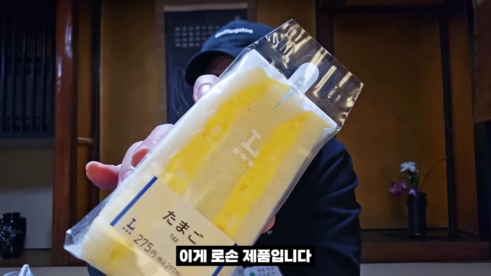 한 사람이 로손 편의점 계란 샌드위치를 카메라 앞으로 들어 보이고 있는 모습이다.