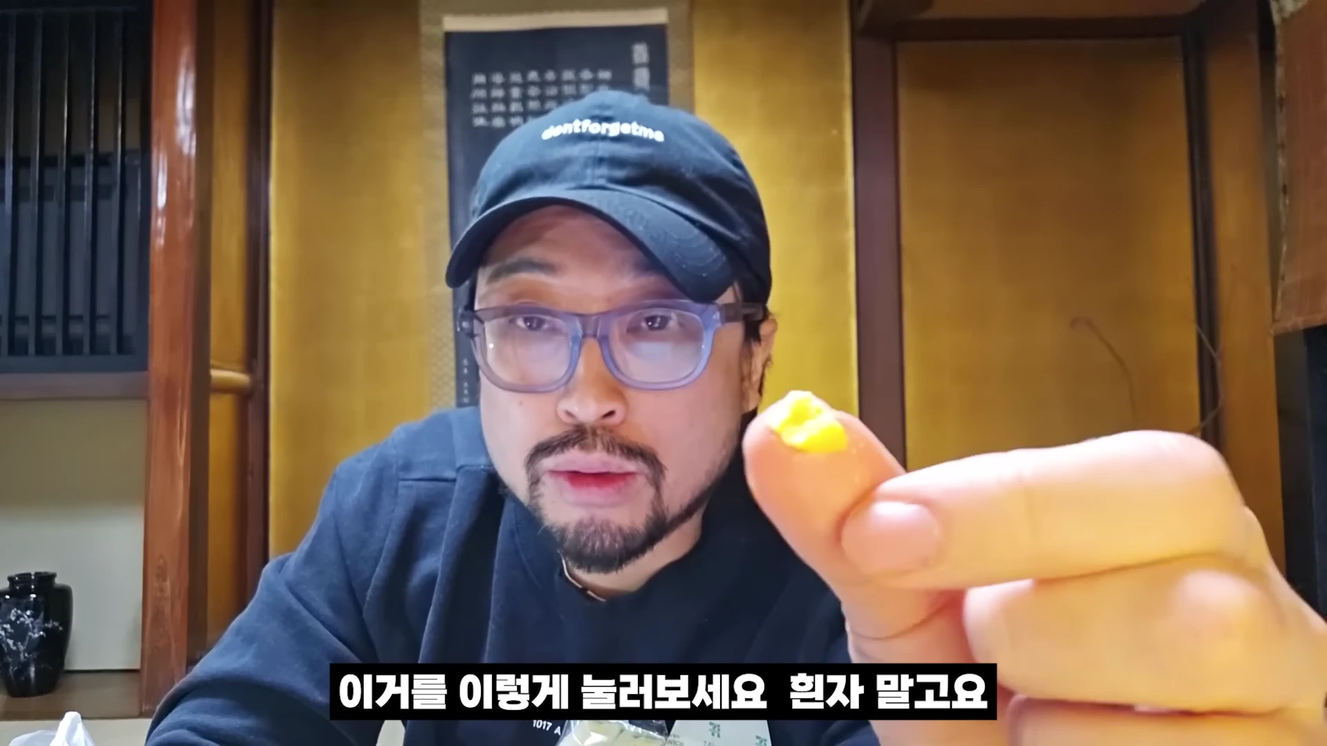 안경과 검은 모자를 쓴 남성이 손가락 끝에 샌드위치 속 노란자 덩어리를 올려 카메라를 향해 보여주고 있다.