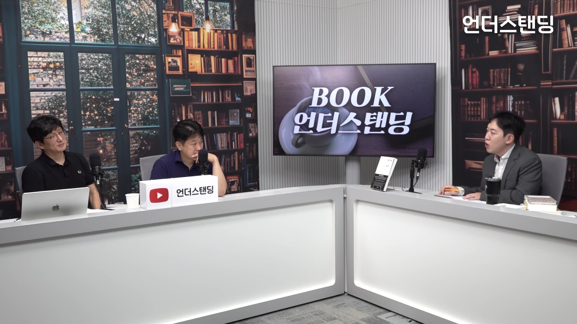 서재 배경의 스튜디오에서 세 명의 남성이 마이크 앞에 앉아 대담을 나누고 있는 모습이다.
