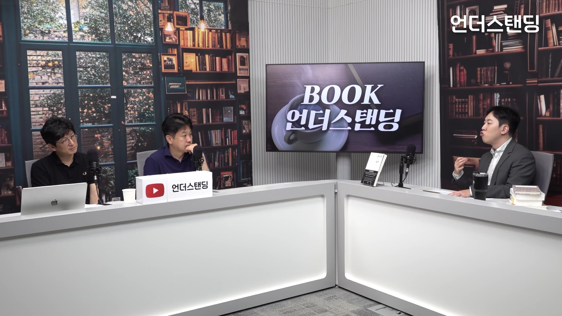 세 명의 남성이 책상에 앉아 마이크를 앞에 두고 대화를 나누고 있는 스튜디오 세트장이며, 배경에는 책장과 'BOOK 언더스탠딩' 로고가 적힌 TV 화면이 보인다.